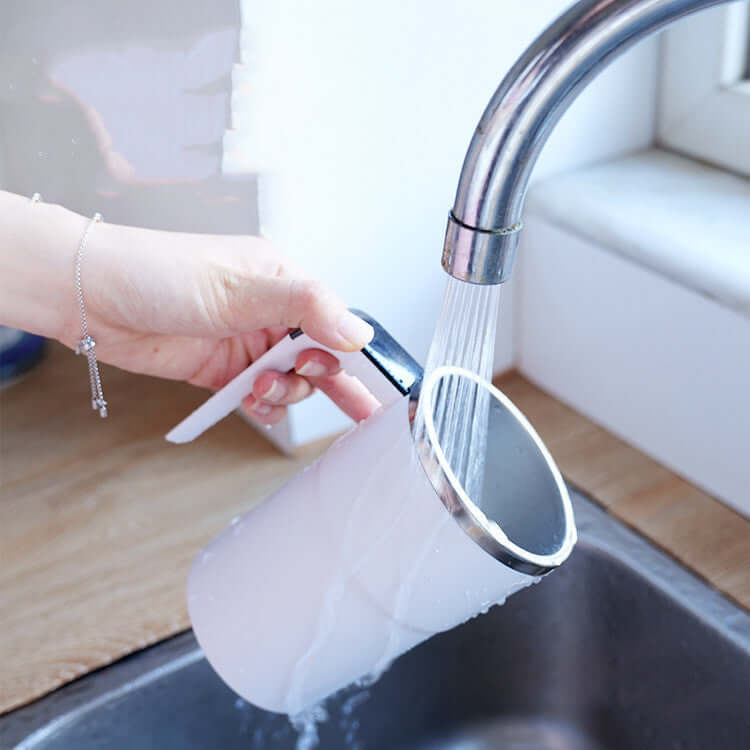 Hand holding a sleek rechargeable electric coffee mug under running water for easy cleaning.