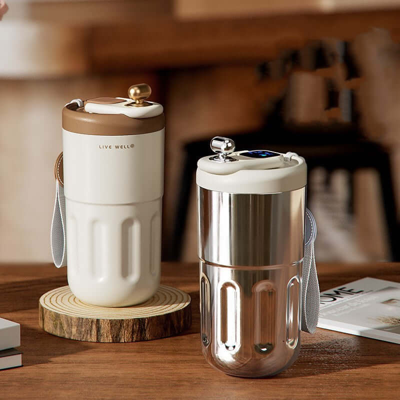Smart stainless steel travel mugs in white and silver on a wooden table, showcasing temperature control features.