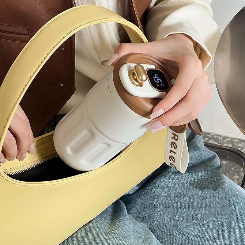 Smart stainless steel travel mug being placed in a stylish yellow bag, displaying temperature control feature.