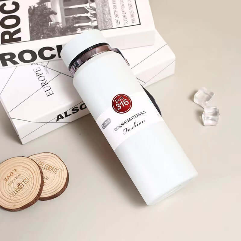 Stylish stainless steel vacuum insulation cup on a table with decorative coasters and a book.